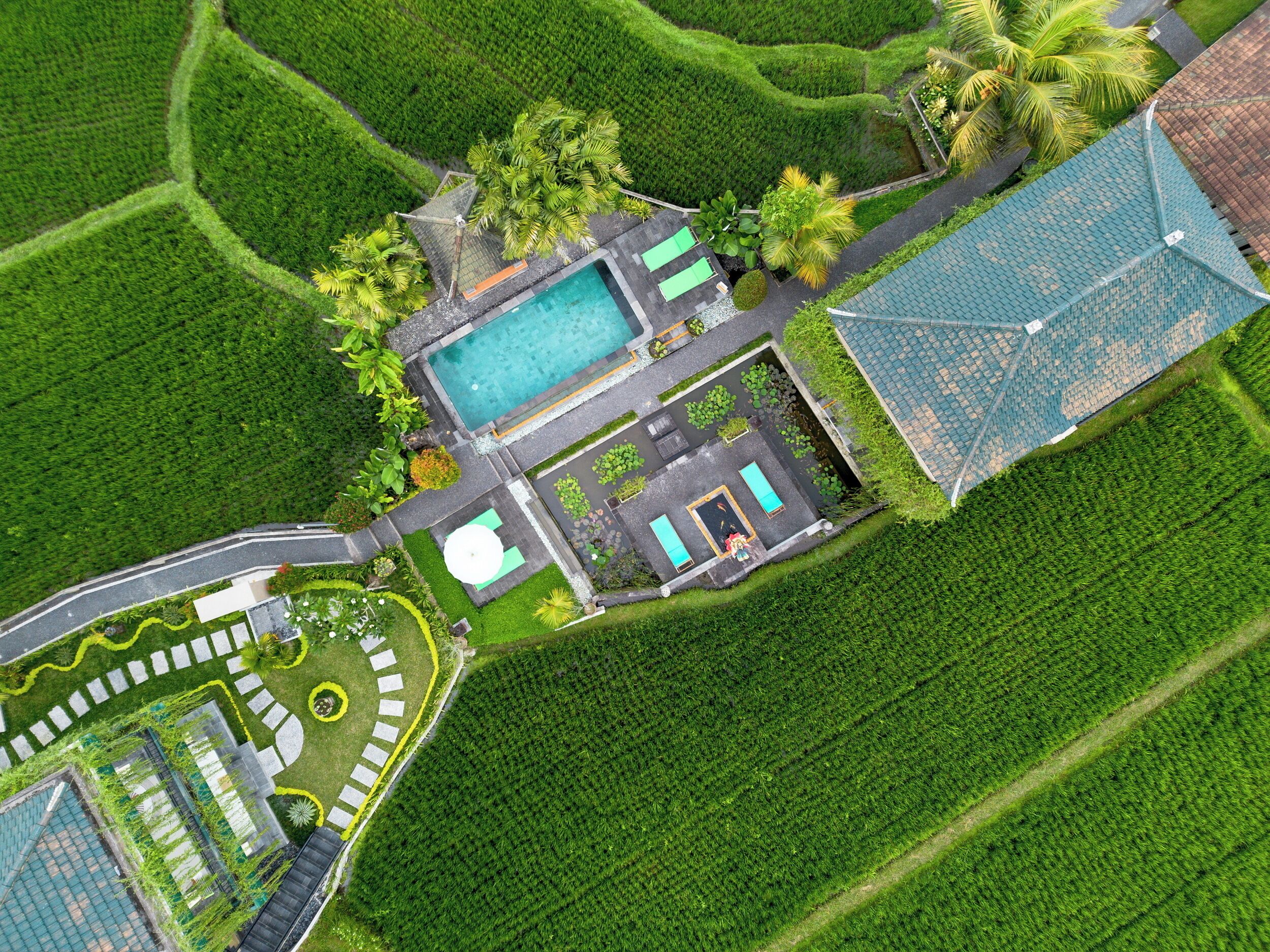 An aerial view of a resort with a swimming pool, a tennis court, and a large building with a blue roof.