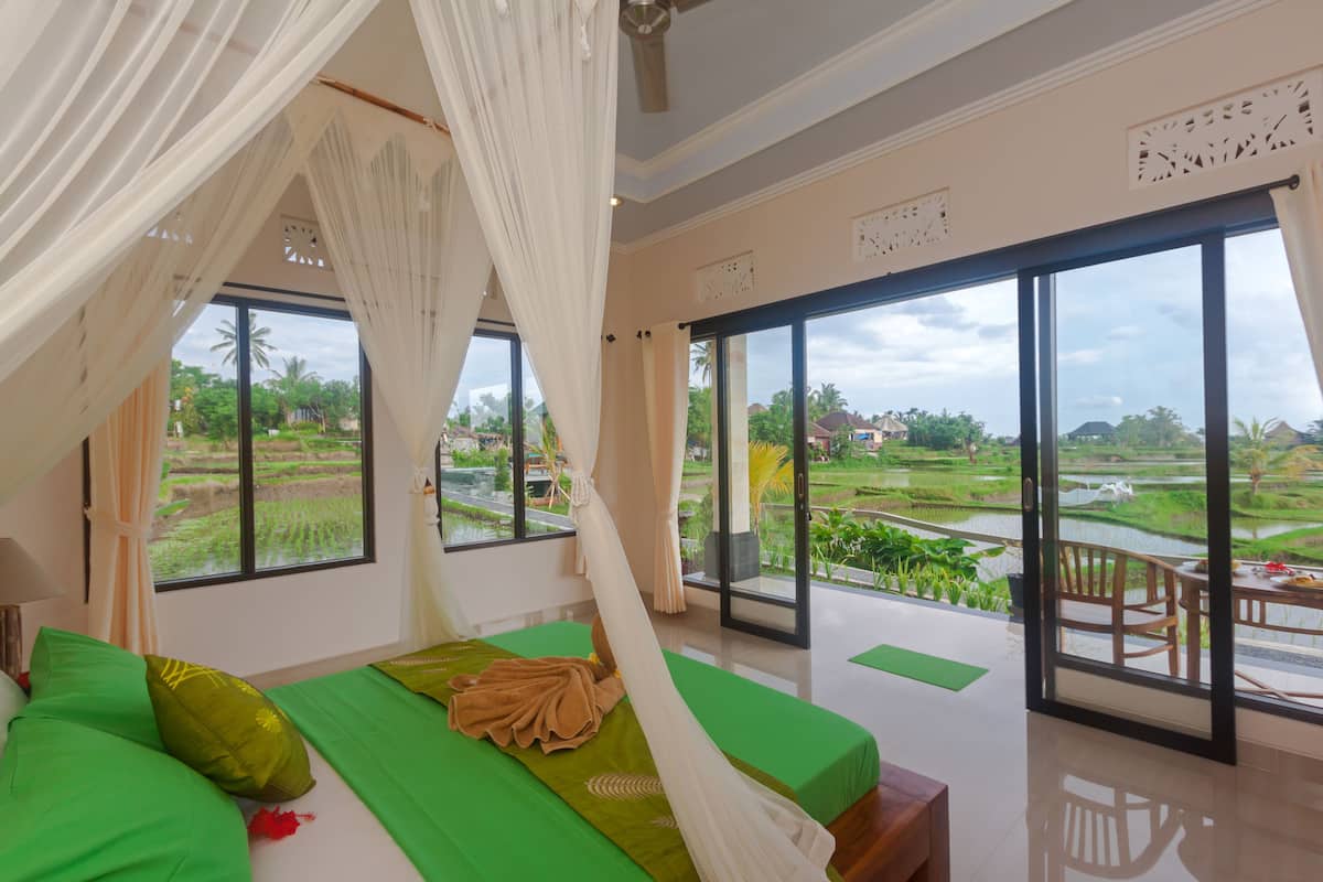 A bedroom with a large bed, a view of the surrounding landscape, and a balcony with a table and chairs.
