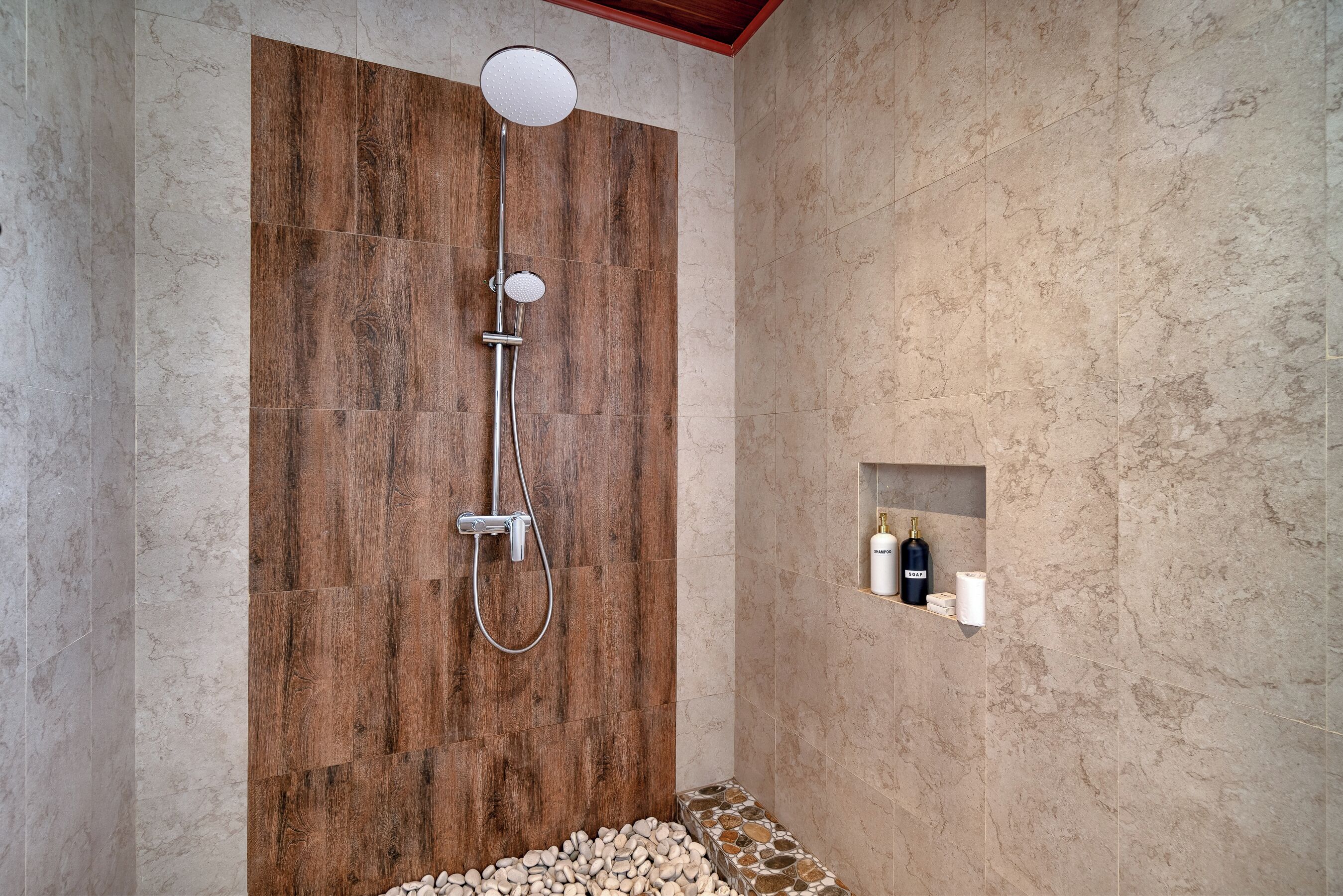 A modern shower area with a wooden panel wall, a marble floor, and a shelf with toiletries.