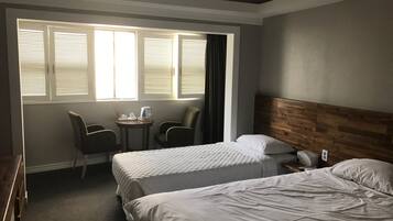 Habitación de hotel con dos camas, una mesita con una tetera y dos sillas.