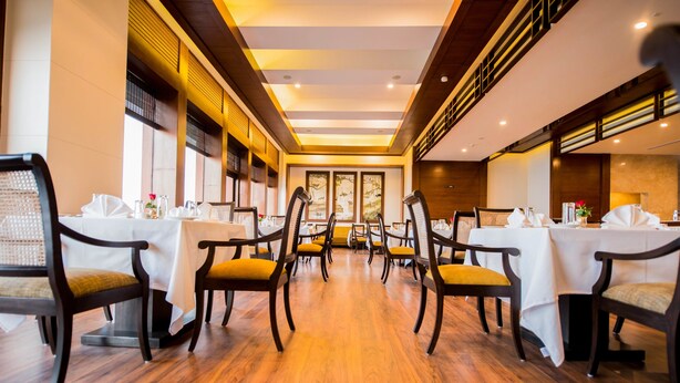 A dining area with wooden flooring, white tablecloths, and dark wooden chairs.