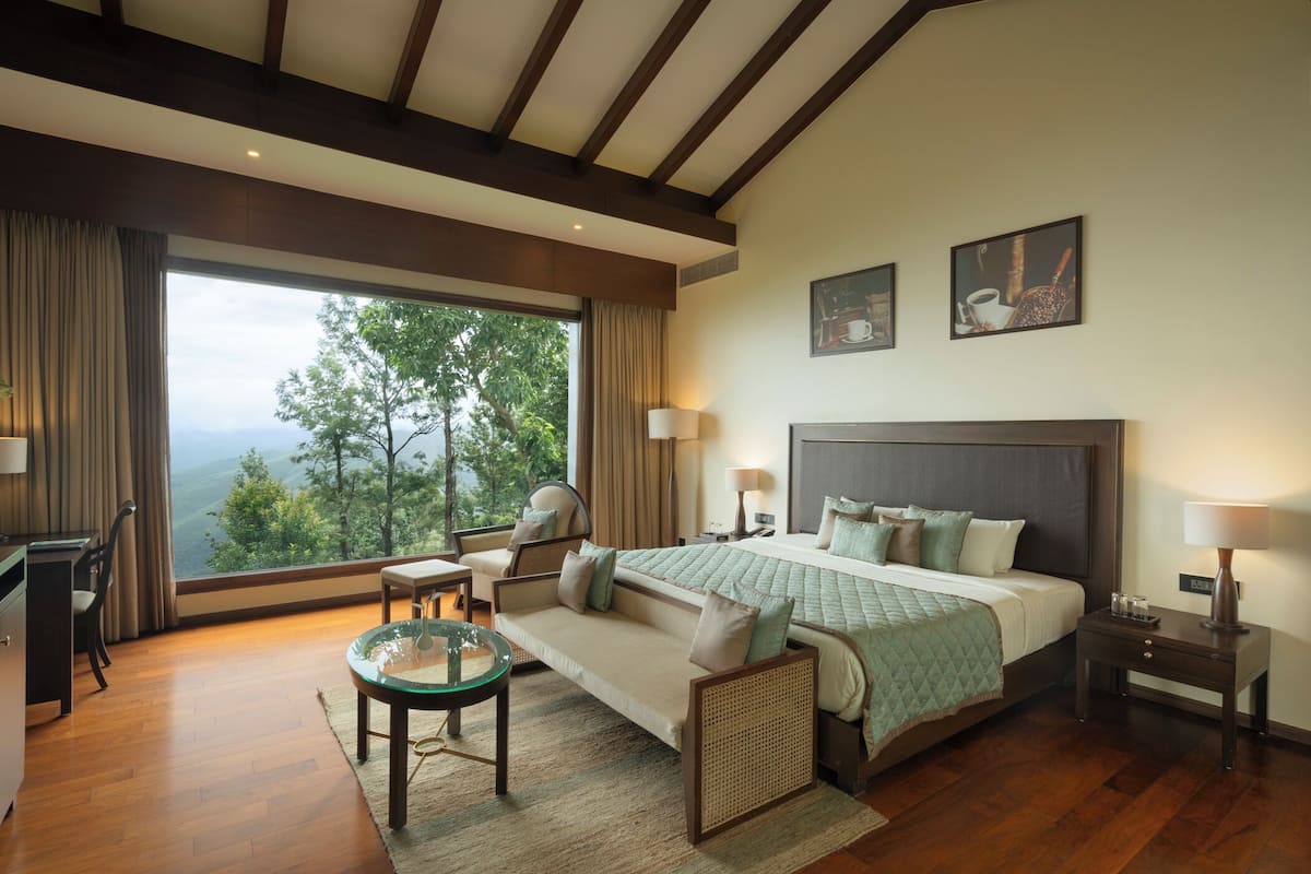 Ein geräumiges Schlafzimmer mit einem großen Bett, einer Sitzecke mit Glastisch und Blick ins Freie.
