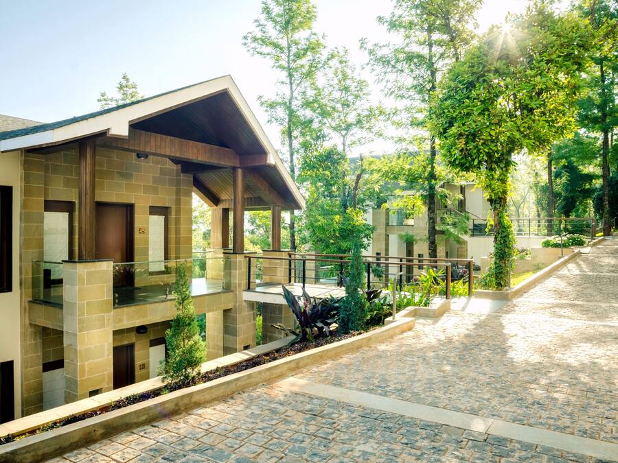 Un edificio moderno con fachada de piedra, un espacio al aire libre cubierto con terraza de madera y un camino pavimentado en piedra.