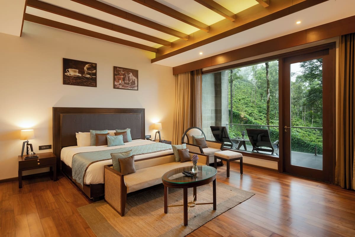 Ein modernes Hotelzimmer mit einem großen Bett, einem Glastisch, einer Couch und einem Balkon mit Blick auf den Wald.