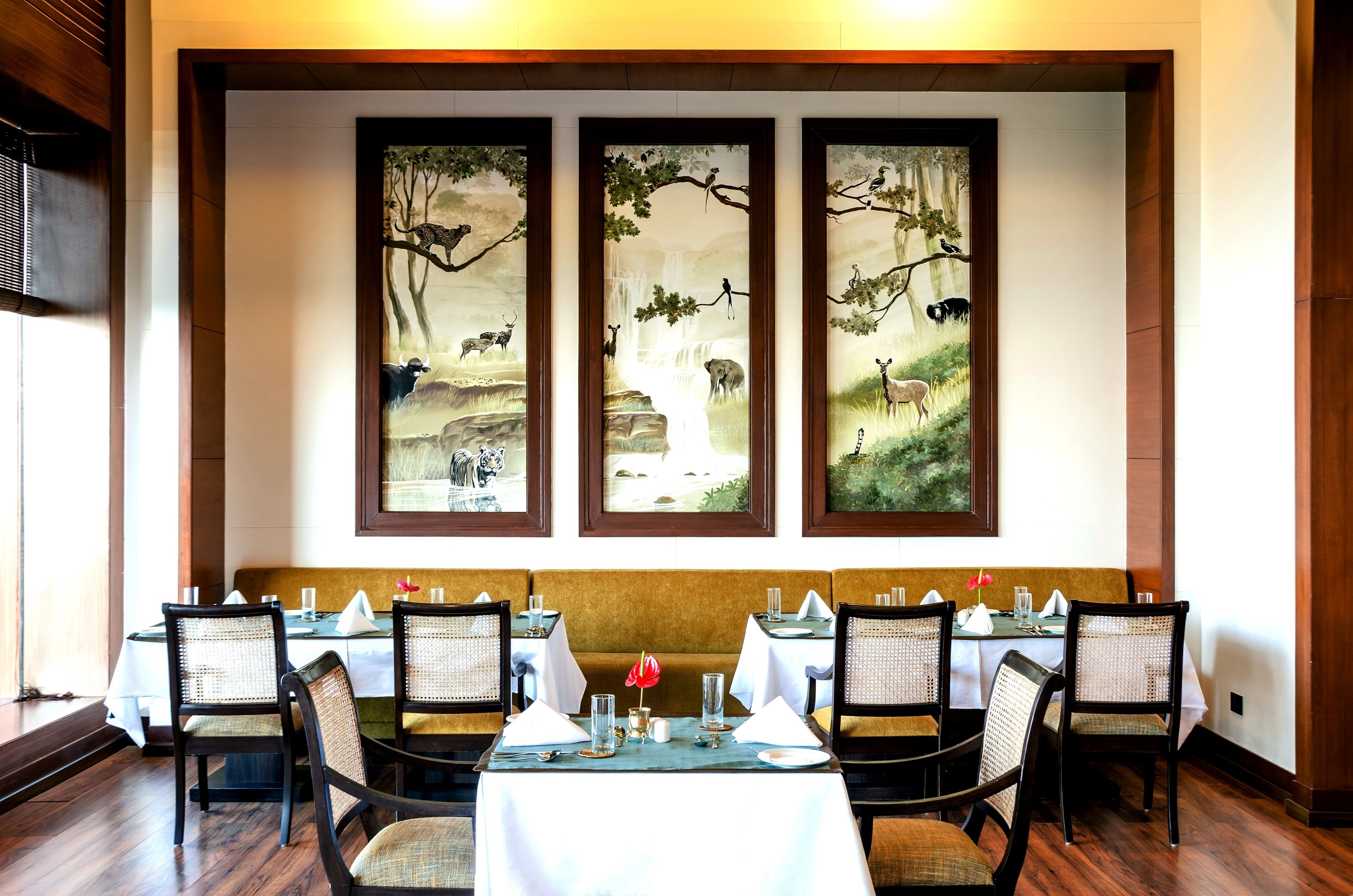 A dining area with tables set for four, each with white tablecloths, chairs, and a central red flower.