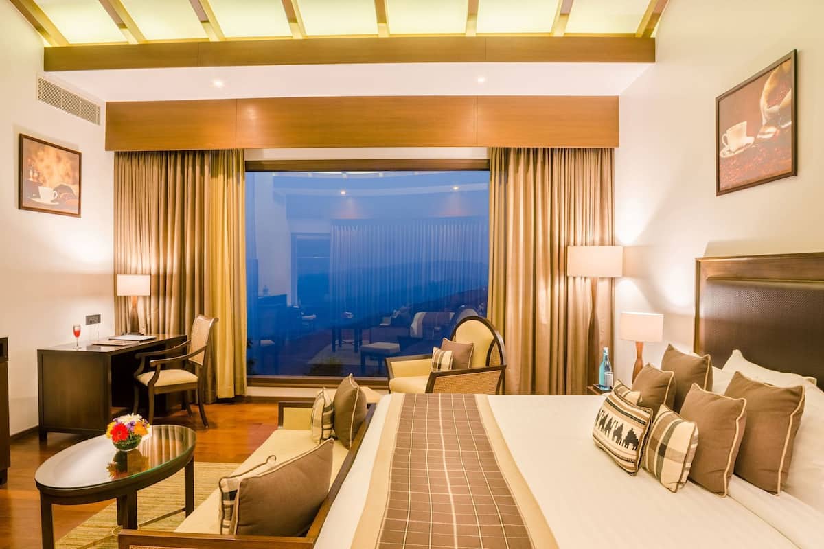 Ein Hotelzimmer mit Bett, Schreibtisch, Stühlen und Blick auf die Stadt, sowie einem großen Fenster.