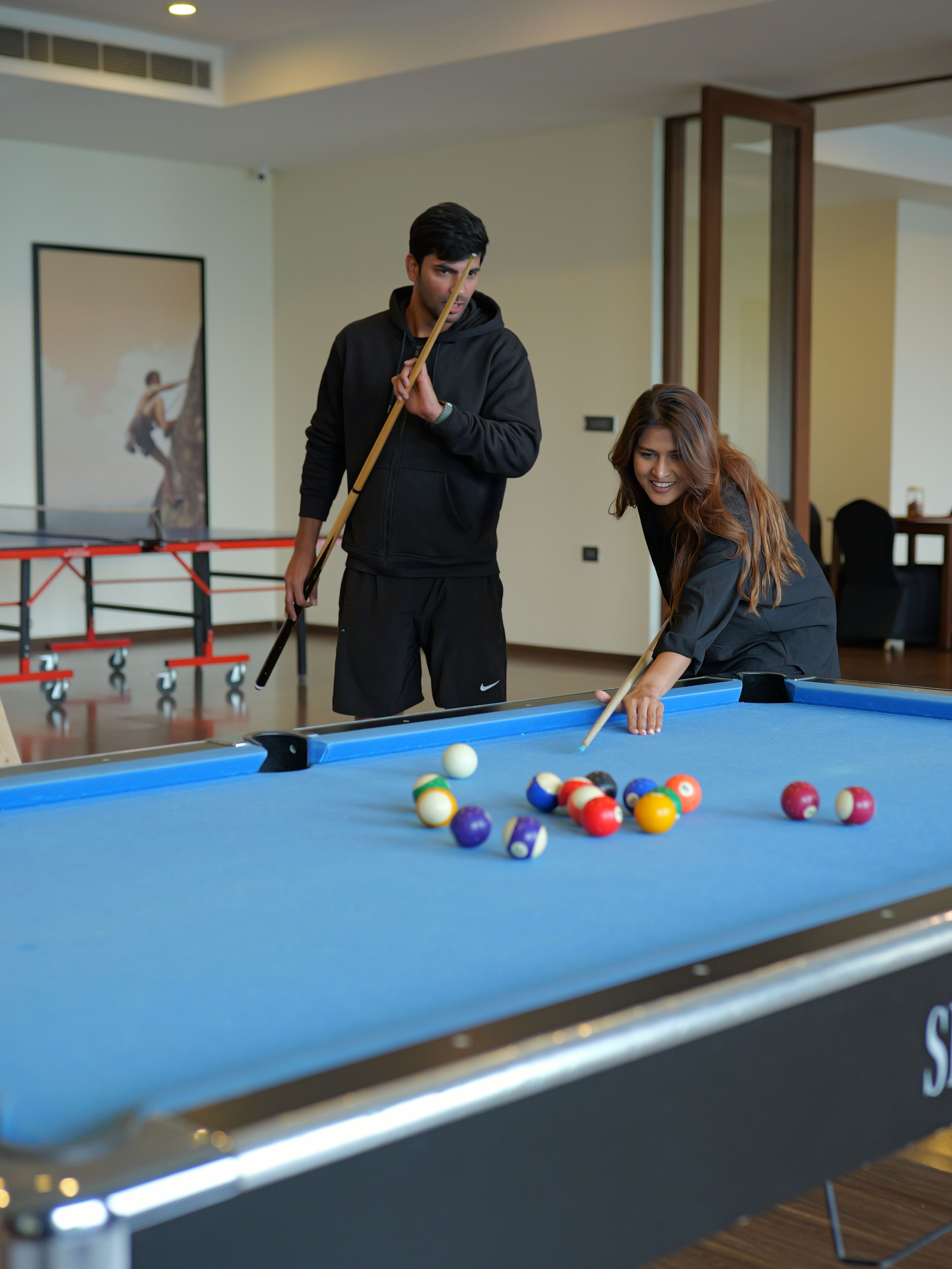A pool table with balls, a person aiming a cue, and a framed picture on the wall.