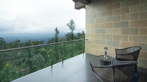 A balcony with a glass railing, two wicker chairs, a small round table, and a vase with flowers. - Trivik Hotels & Resorts, Chikmagalur (Chikkamagaluru)