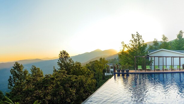 A pool with a view of mountains, a covered seating area, and a modern building. - Trivik Hotels & Resorts, Chikmagalur (Chikkamagaluru)