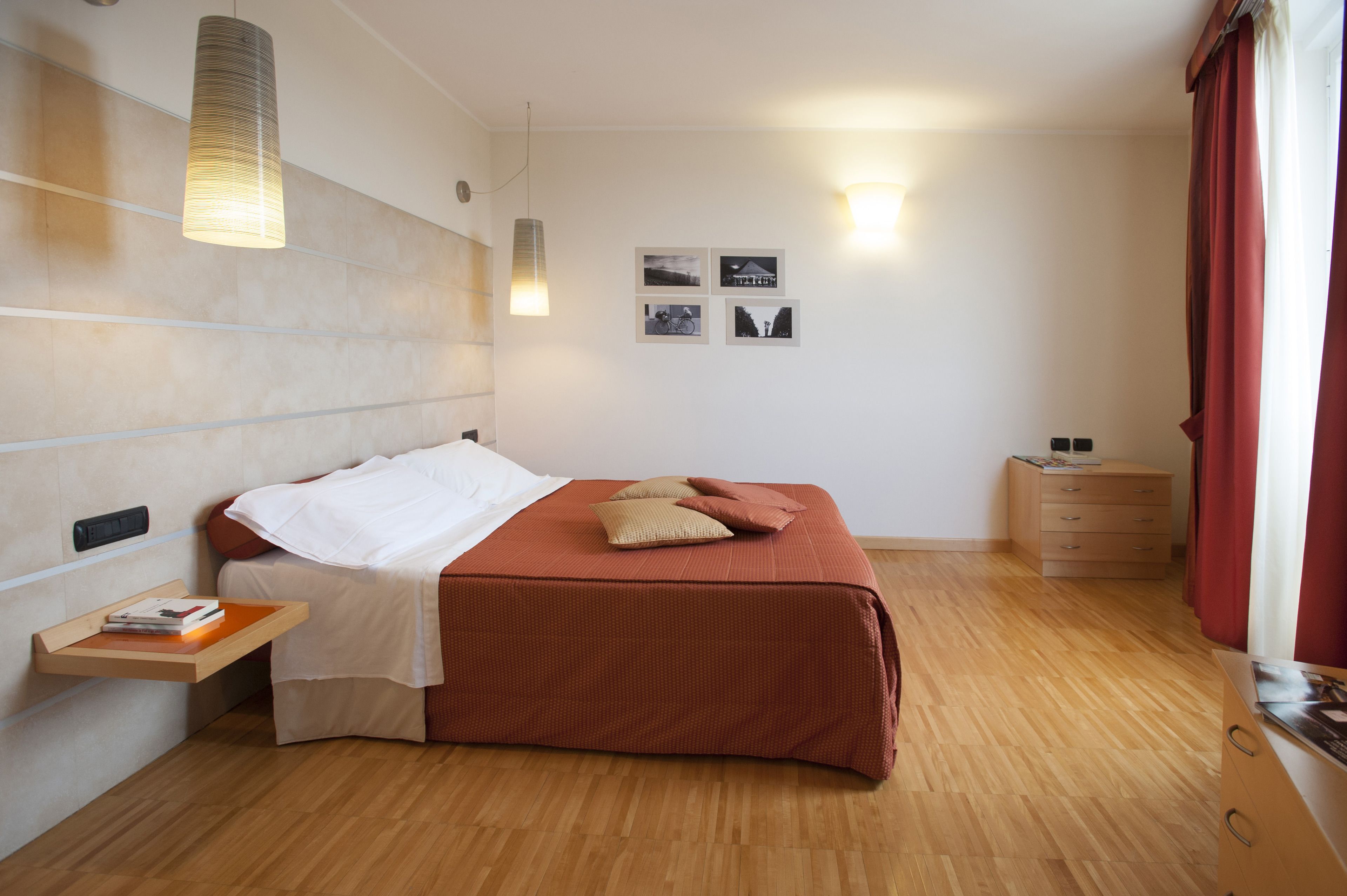 A bedroom with a bed, bedside table, wall-mounted light, and a dresser.