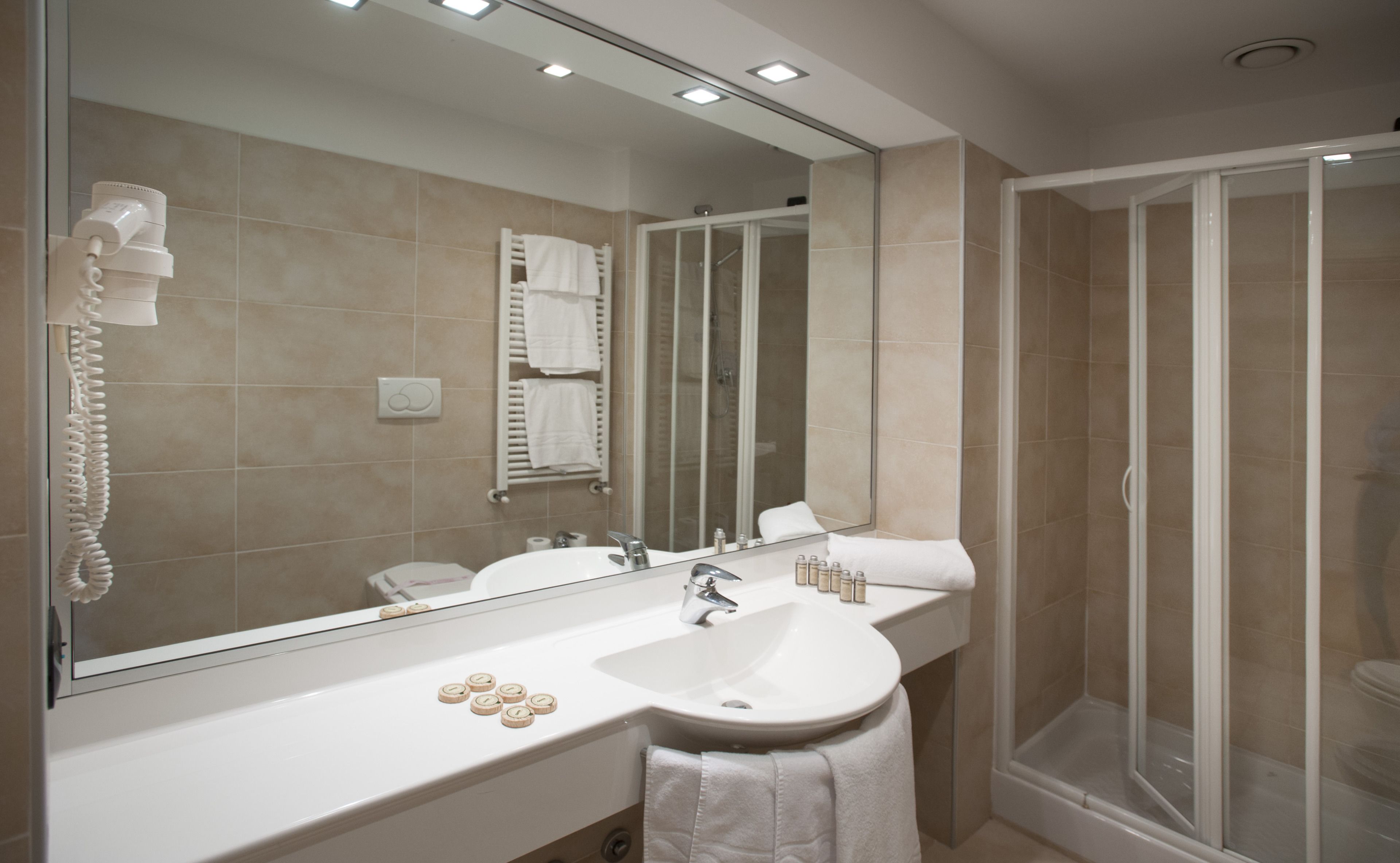 A modern bathroom with a large mirror, a sink, a shower, and a telephone.