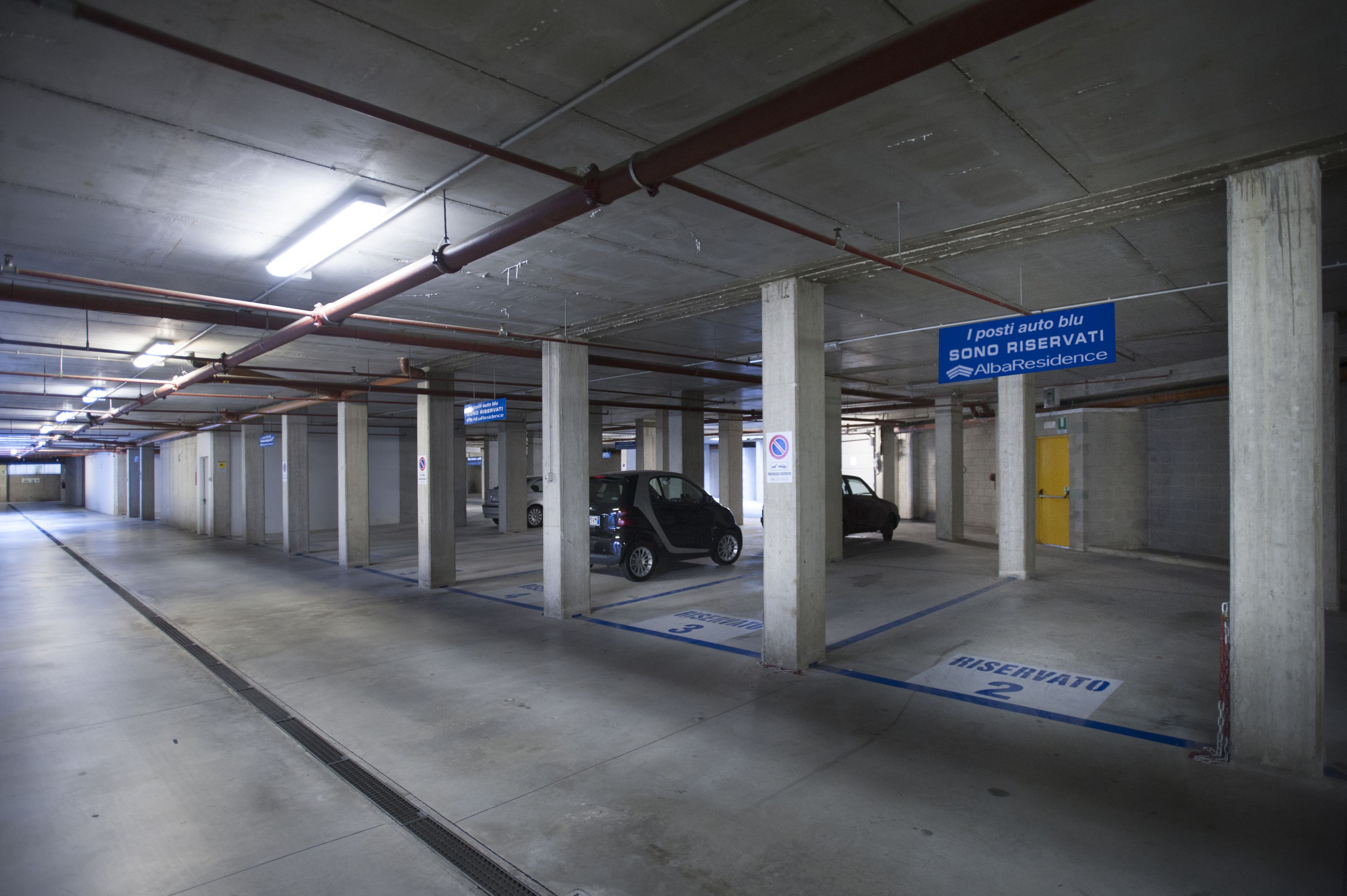 A parking garage with concrete pillars, a blue sign indicating reserved parking, and a small car parked in a reserved space.
