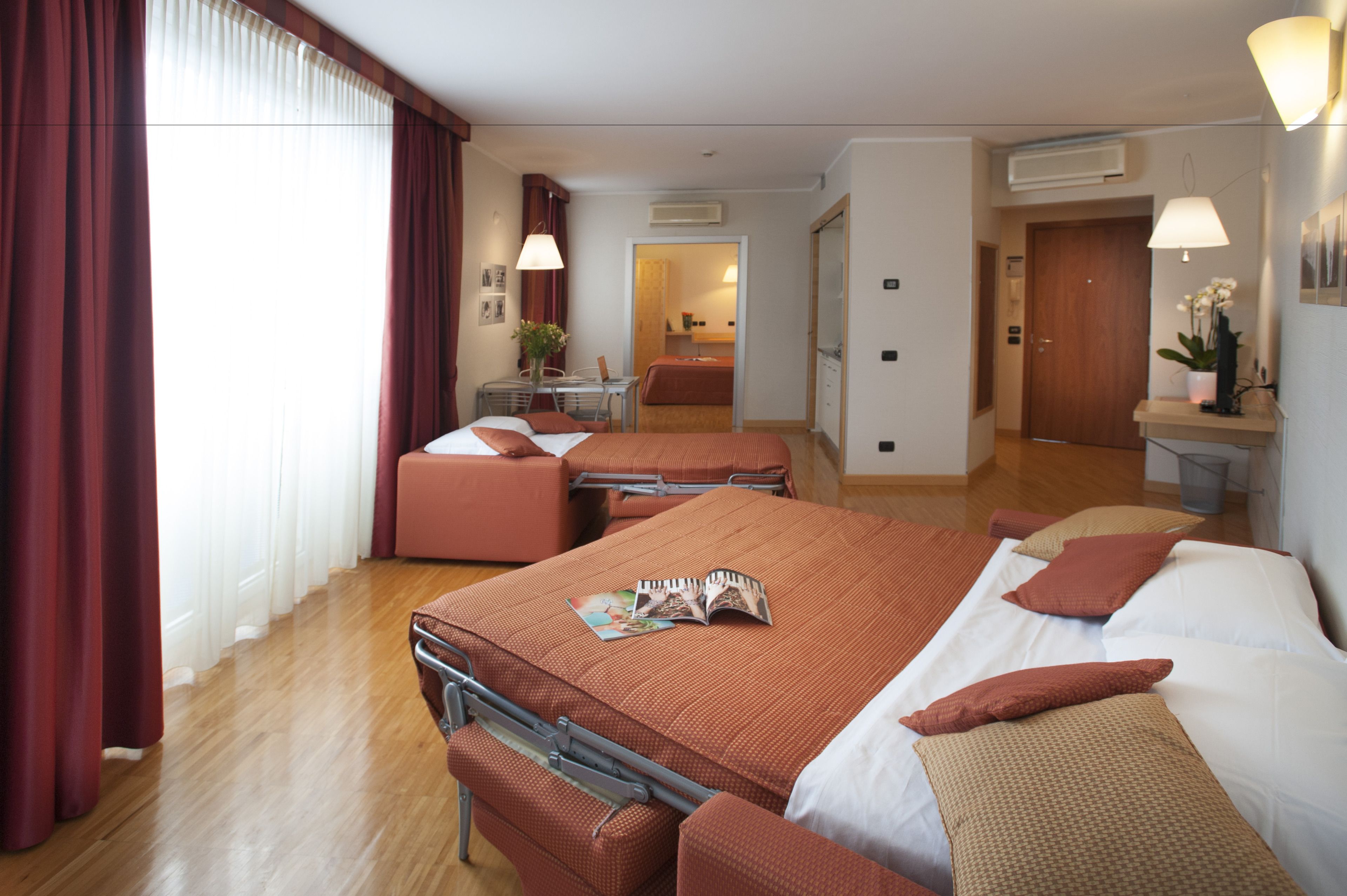 A hotel room with a large bed, two smaller beds, a desk, and a bathroom visible through an open door.