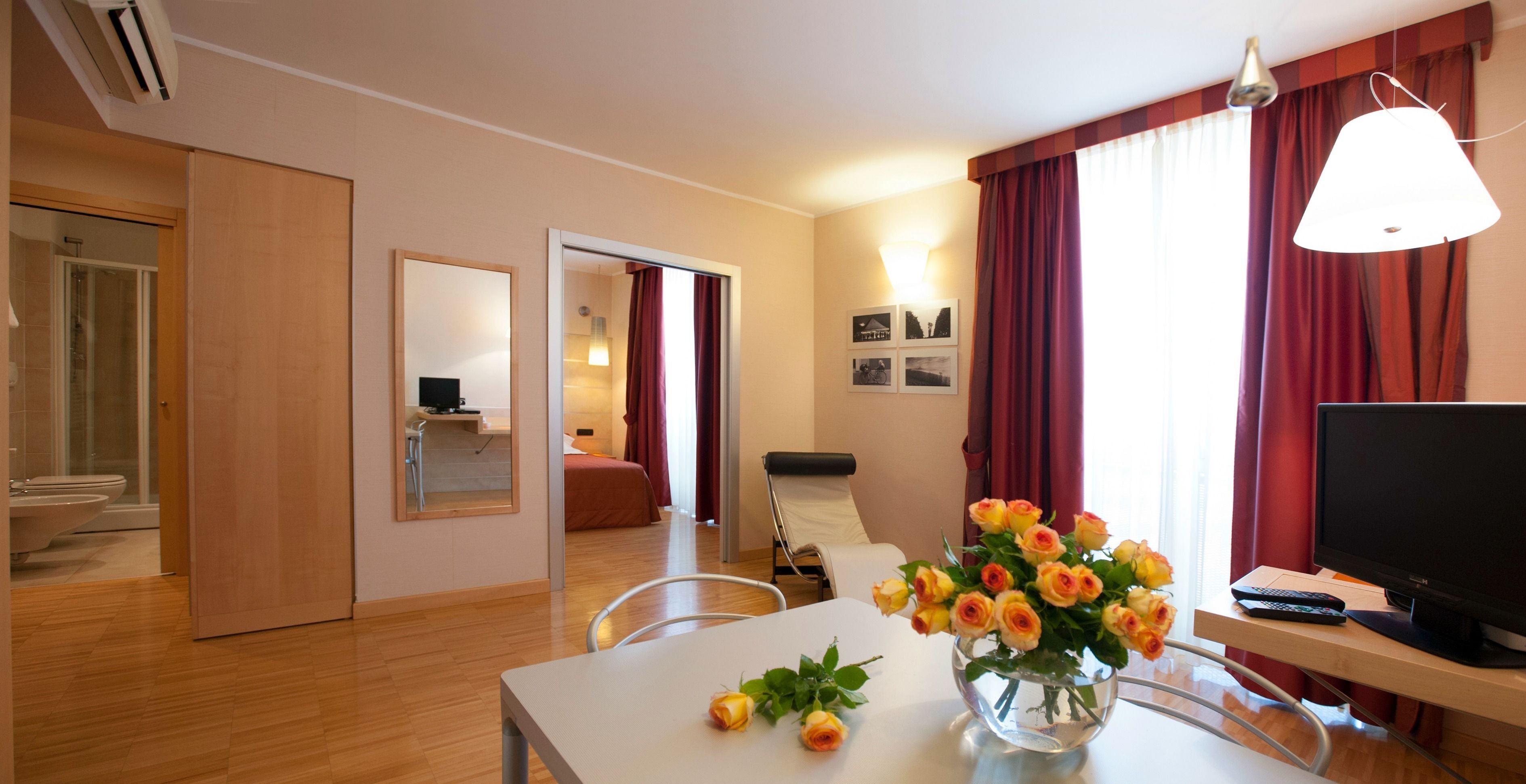 Quarto de hotel com área de refeições, televisão e um vaso de flores.
