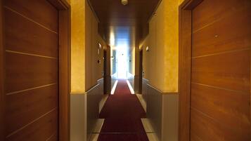 A hotel hallway with wooden doors on both sides, a red carpet, and a light at the end of the corridor.