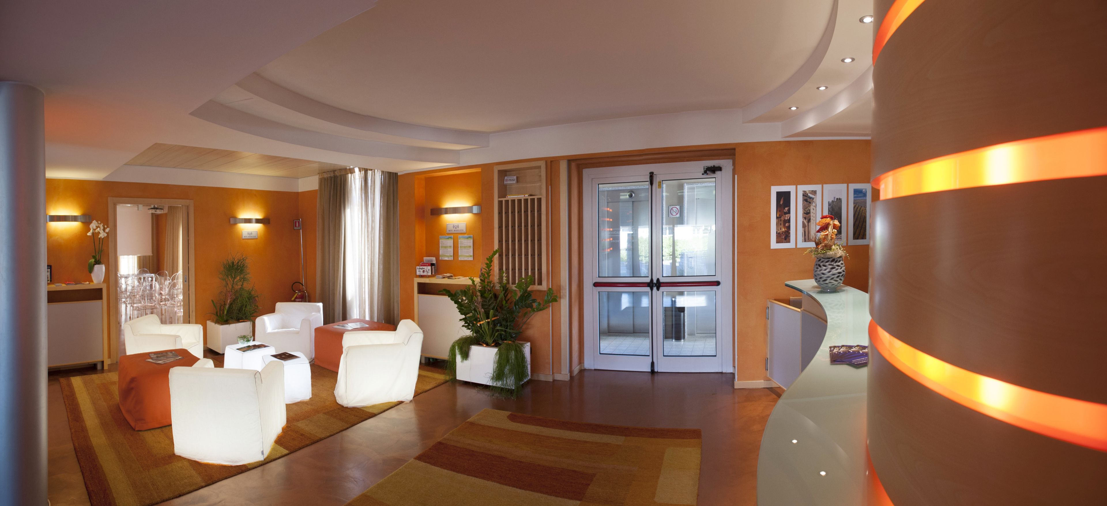A modern hotel lobby with white furniture, a reception desk, and a large mirror.