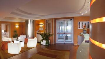 A modern hotel lobby with white furniture, a reception desk, and a large mirror.