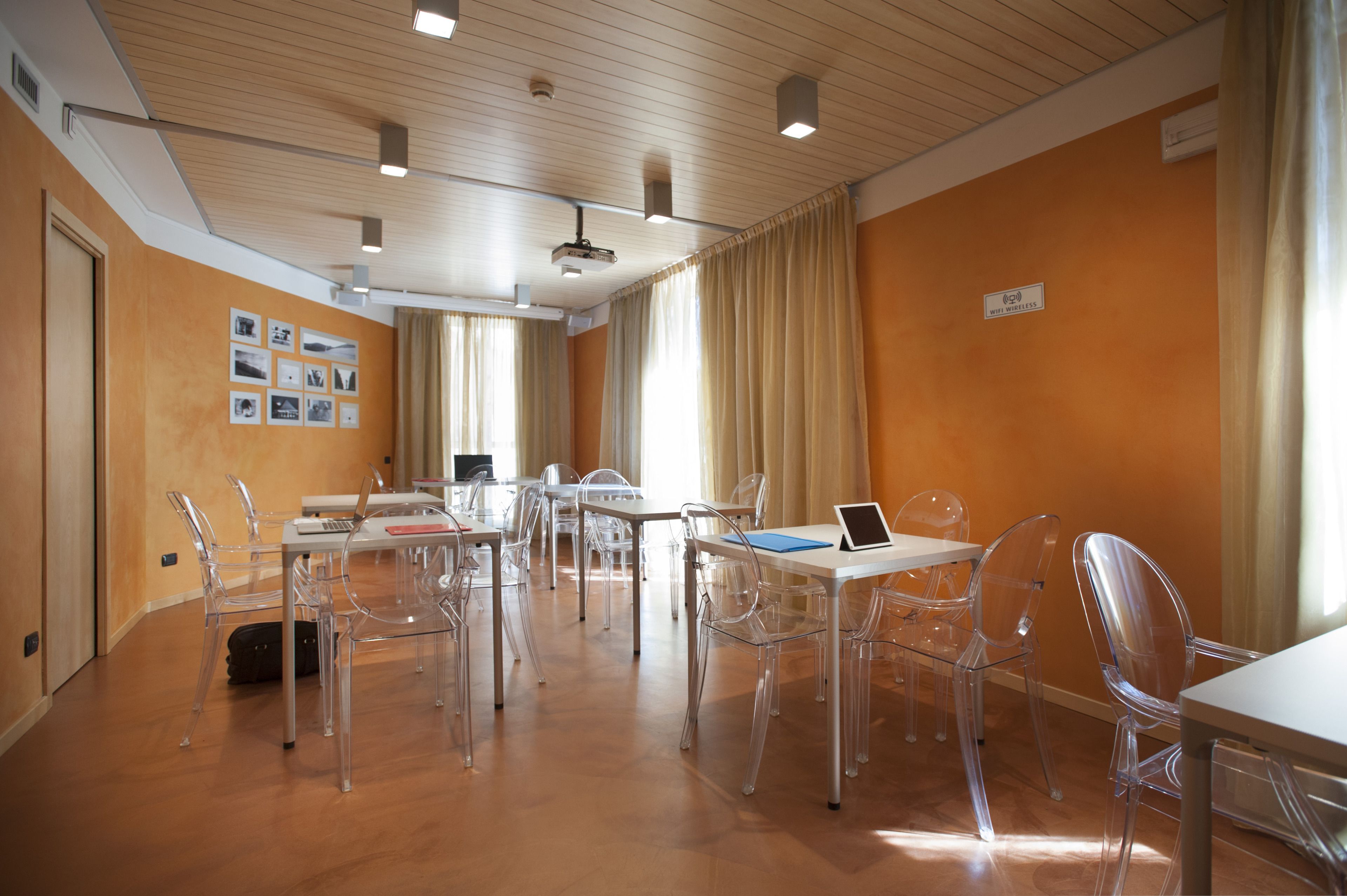 Une salle de conférence avec des chaises en plastique transparent, des tables blanches et un projecteur fixé au plafond.