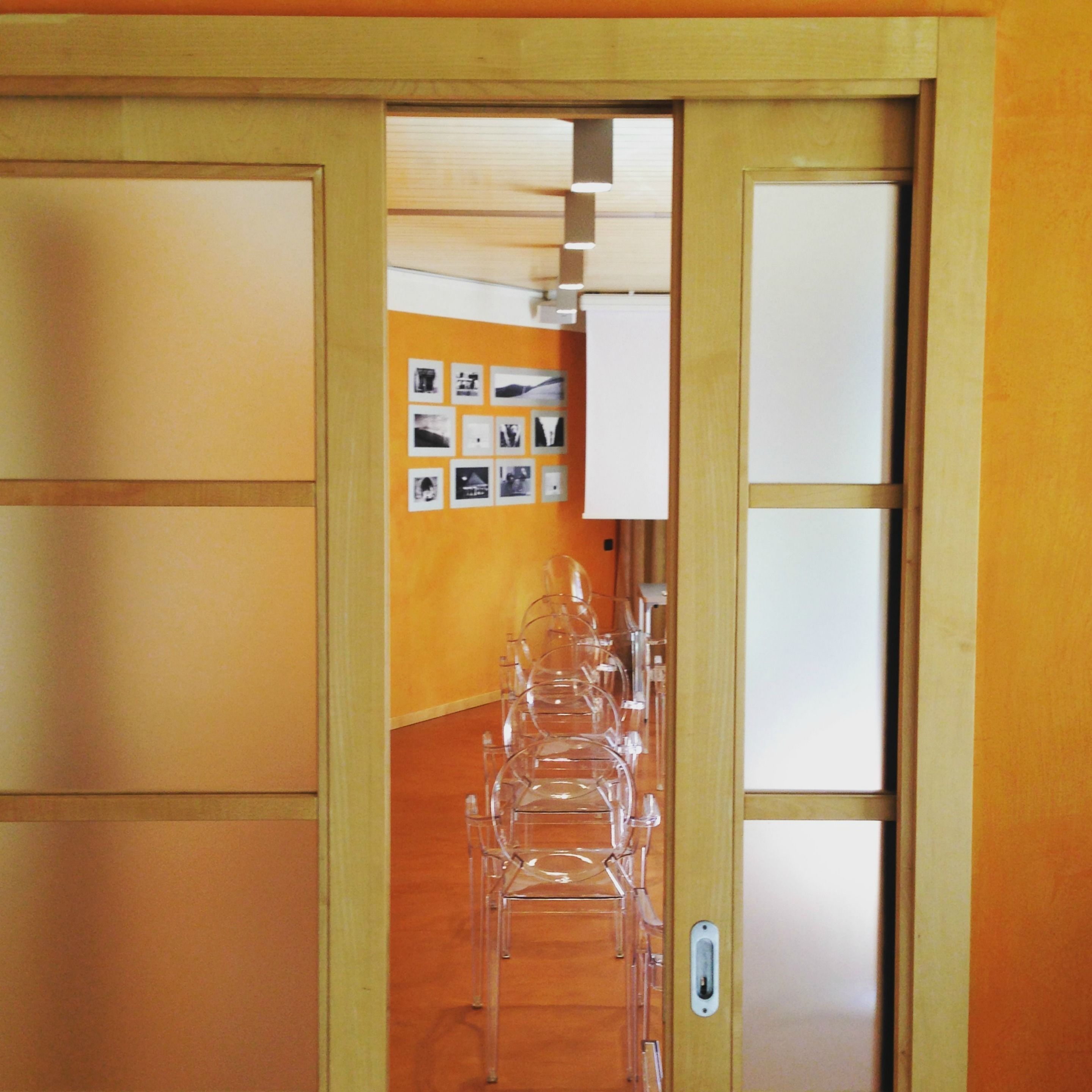 Una habitación con piso de madera, una puerta con paneles de vidrio esmerilado y una pared decorada con cuadros.