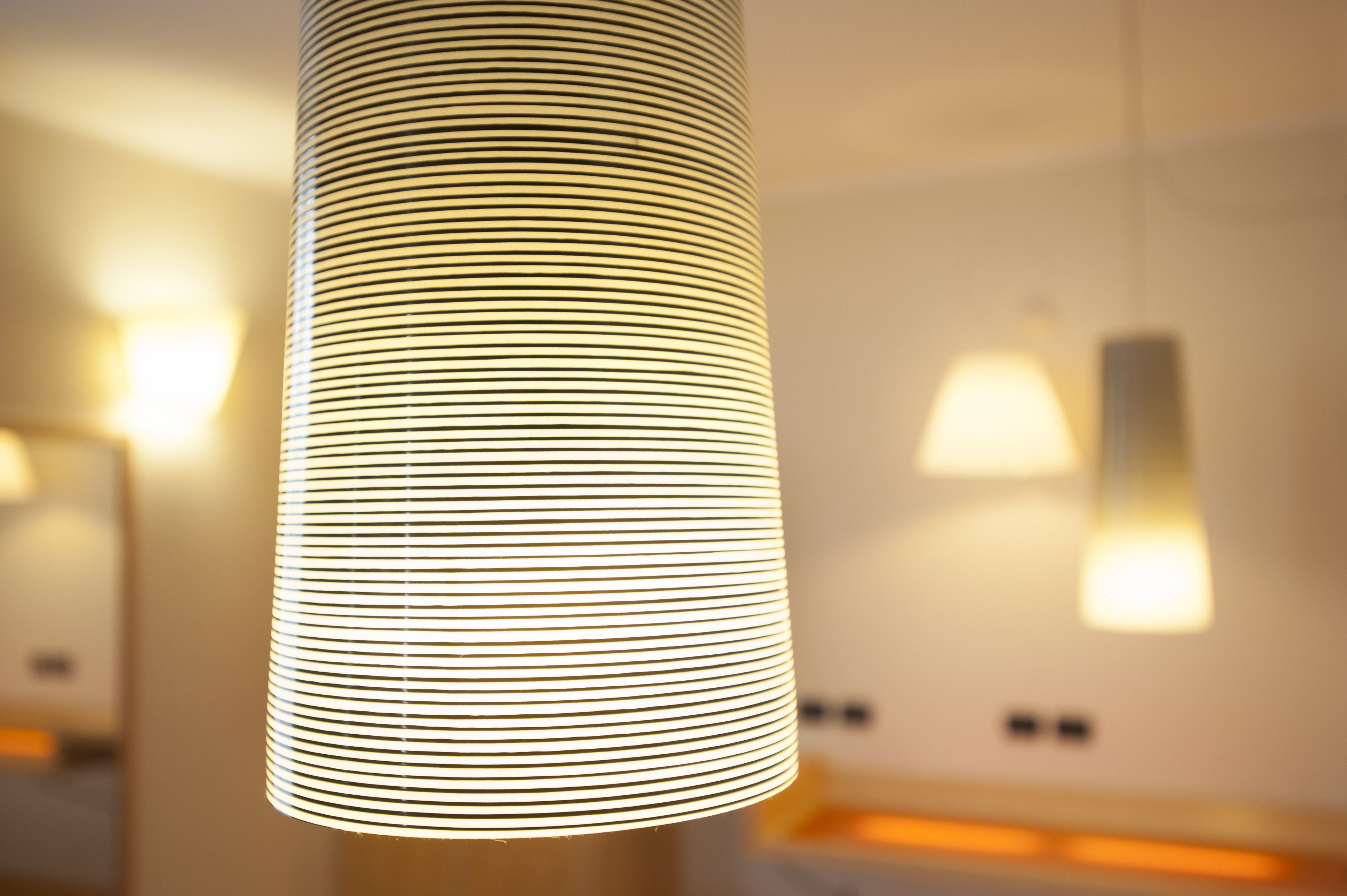Un luminaire cylindrique orné de lignes horizontales, suspendu dans une pièce bien éclairée et dotée d’un design moderne.