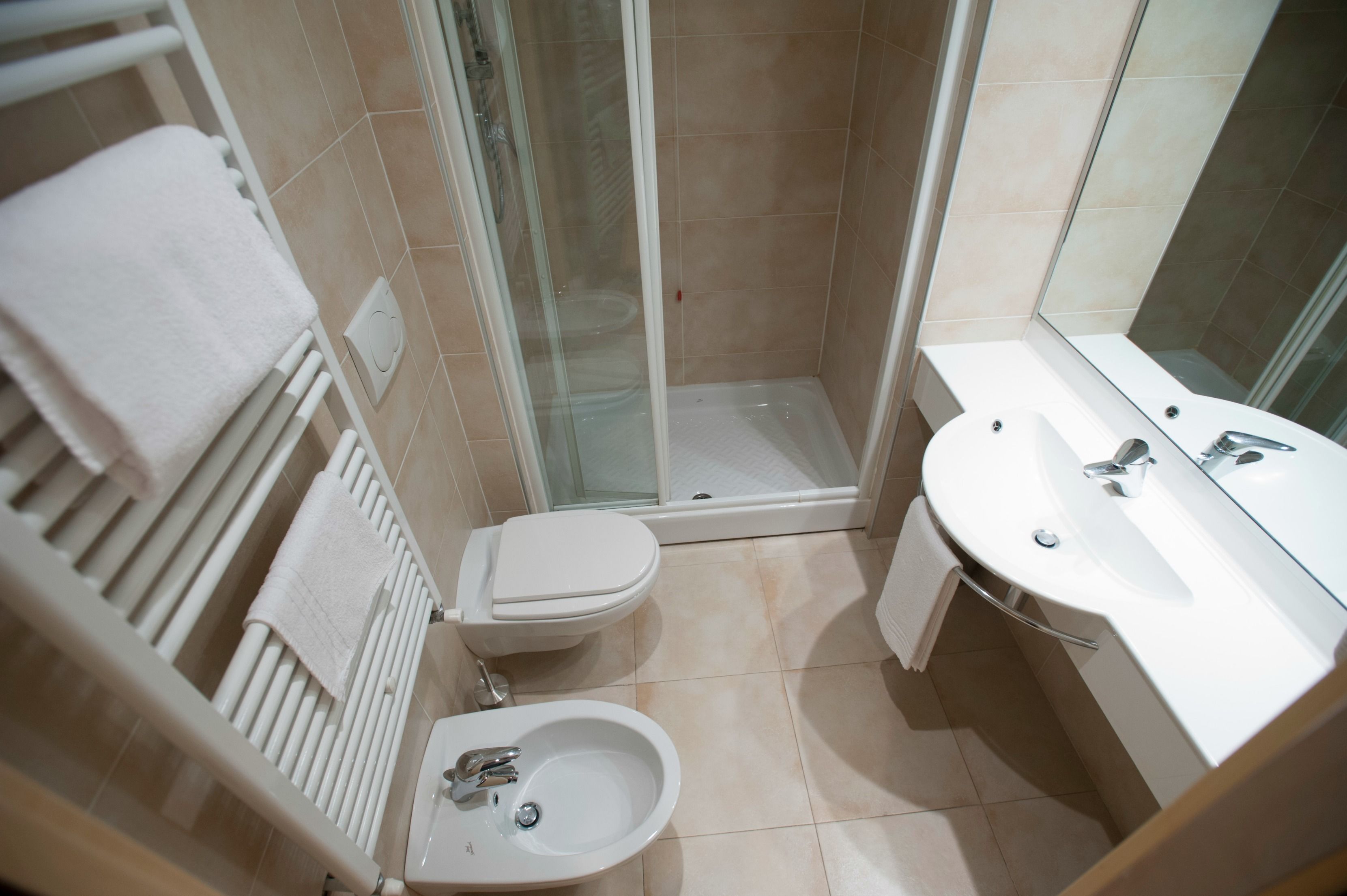 A bathroom with a shower, toilet, bidet, and a sink.