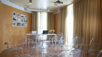 A conference room with clear plastic chairs, a table with a laptop, and a projector on the ceiling.