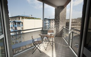 A balcony with a laptop on a small table, a chair, and a view of buildings in the background.