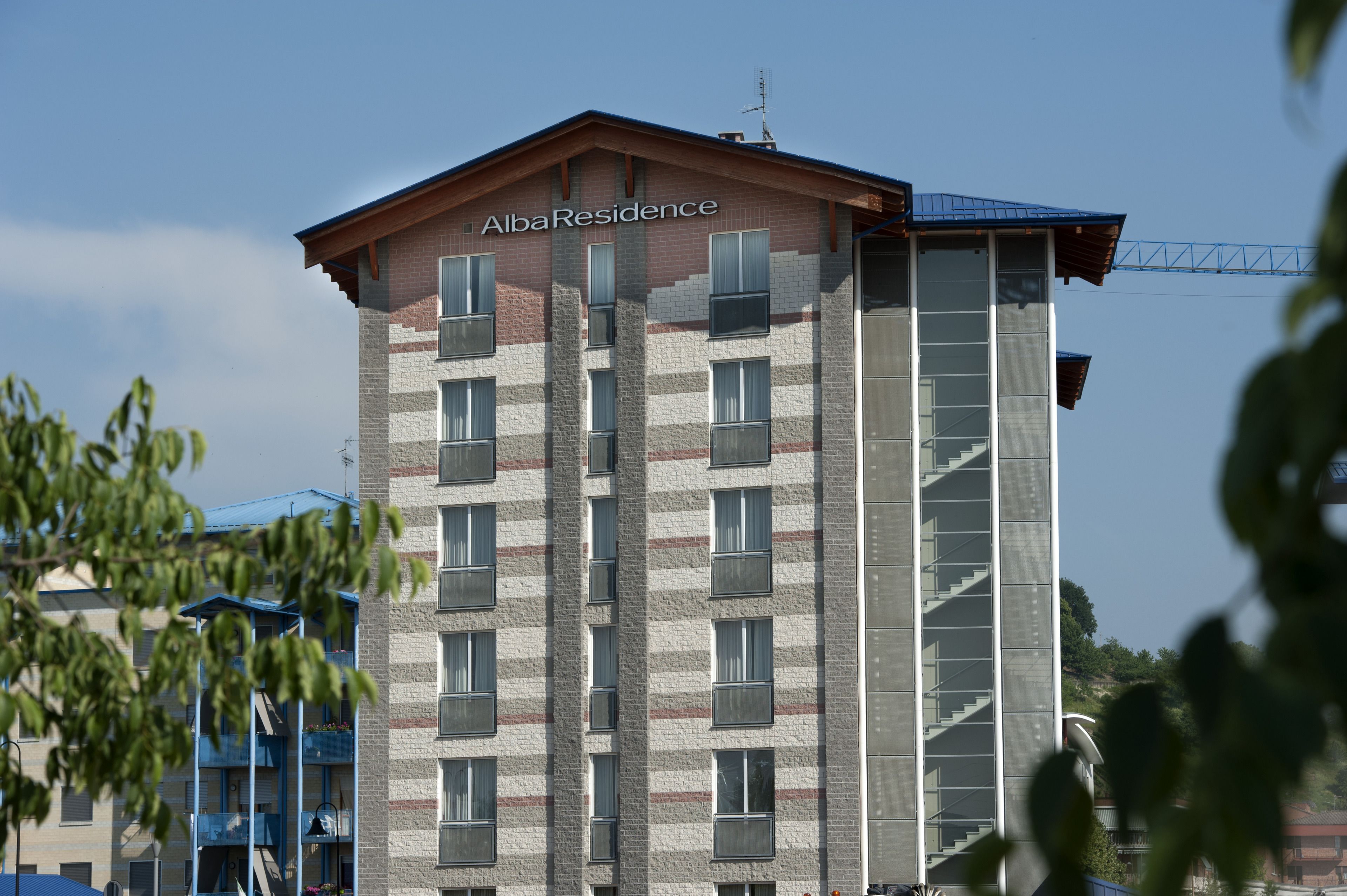 A multi-story building with the name "AlbaResidence" on the facade. It features a mix of brick and glass windows, a visible staircase on the right side, and balconies on the left.