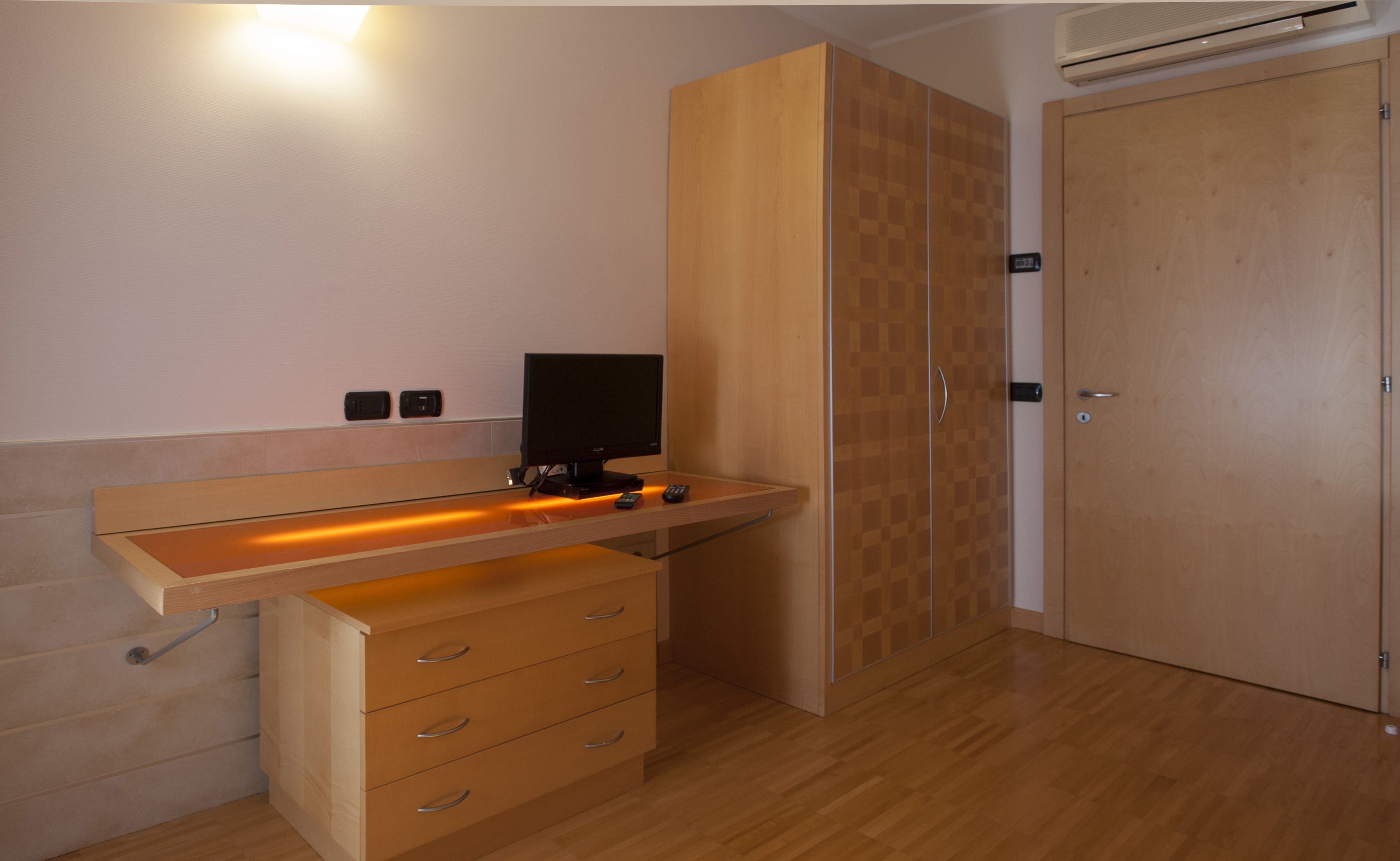 Une chambre avec un bureau en bois, une télévision et une armoire.