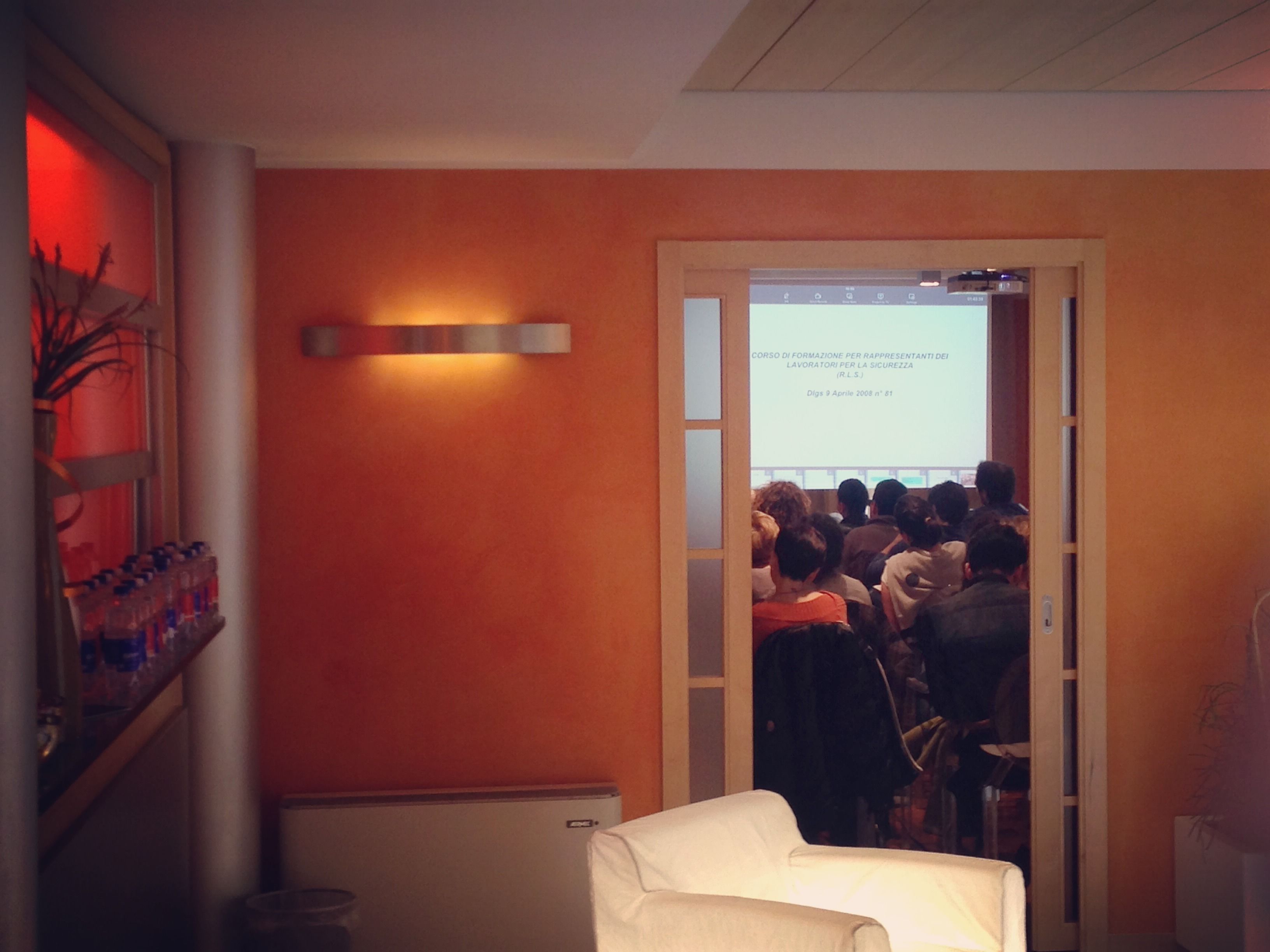 A conference room with an orange wall, a white chair, and a projection screen displaying a presentation.