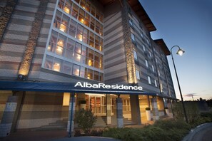 A multi-story building with a prominent entrance, large windows, and a sign reading "AlbaResidence."