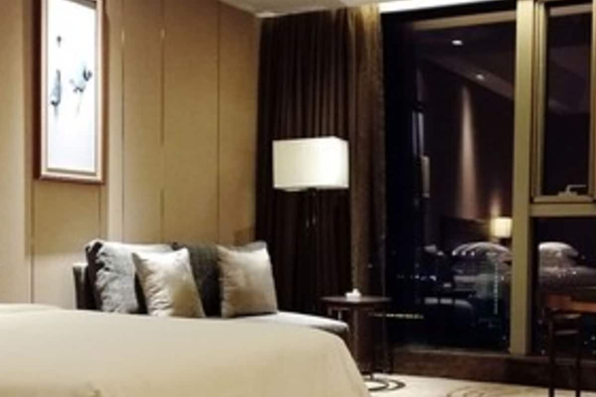 Habitación de hotel con una cama grande, una mesita de noche, una lámpara y vista a la ciudad de noche.