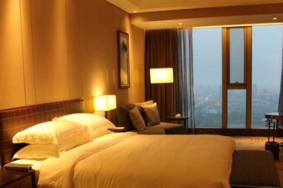 Habitación de hotel con una cama grande, un escritorio, una silla y vistas a la ciudad a través de la ventana.