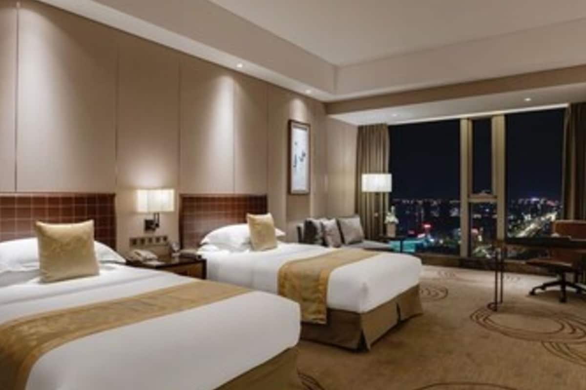 Habitación de hotel con dos camas, una mesita de noche, un escritorio y un ventanal con vista a la ciudad.