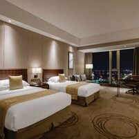 Habitación de hotel con dos camas, una mesita de noche, un escritorio y un ventanal con vista a la ciudad.