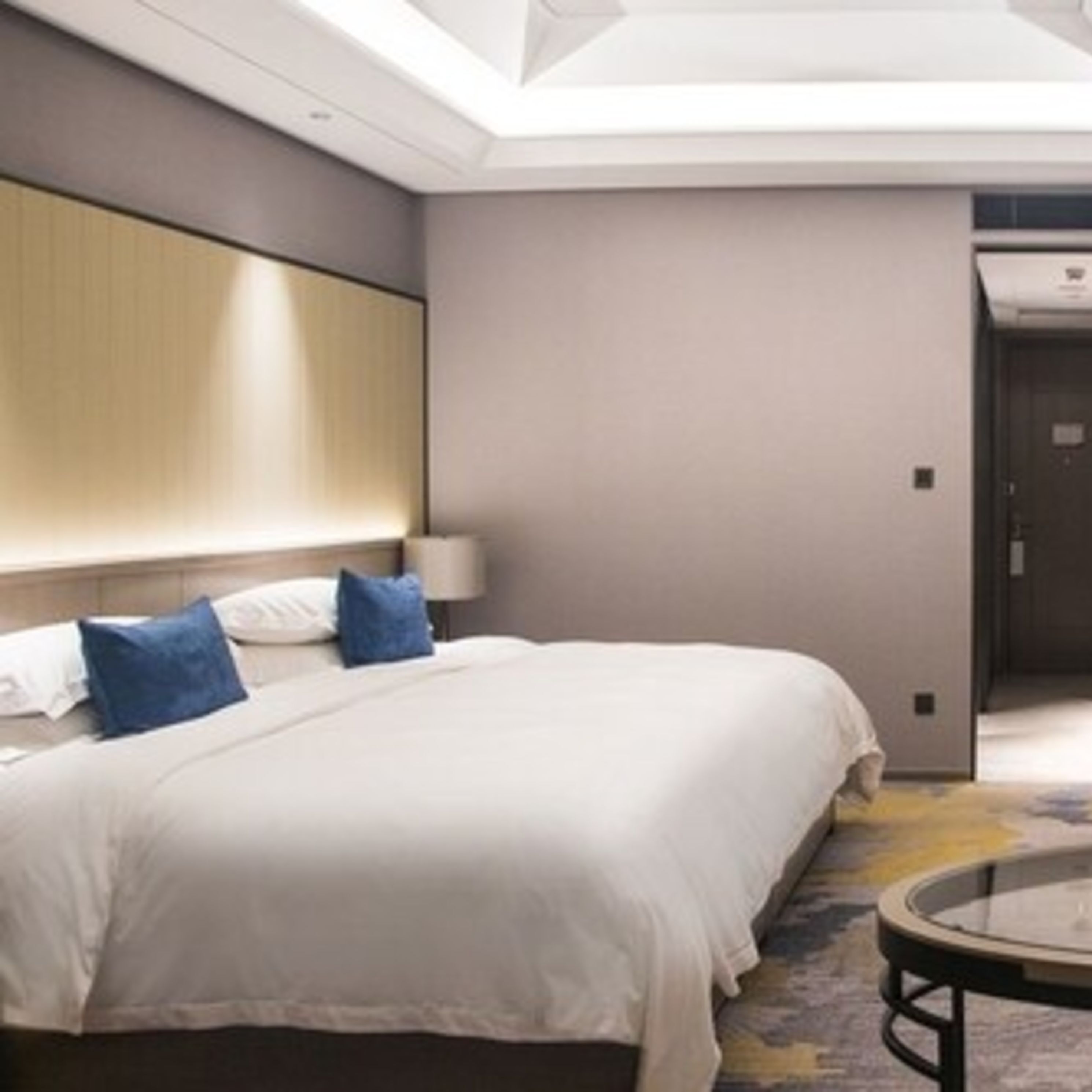 Una habitación de hotel con una cama grande, una mesita de noche y una mesa redonda de vidrio.