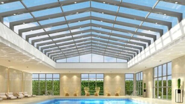 Una piscina interior con techo de cristal, varias tumbonas y vistas despejadas al exterior.