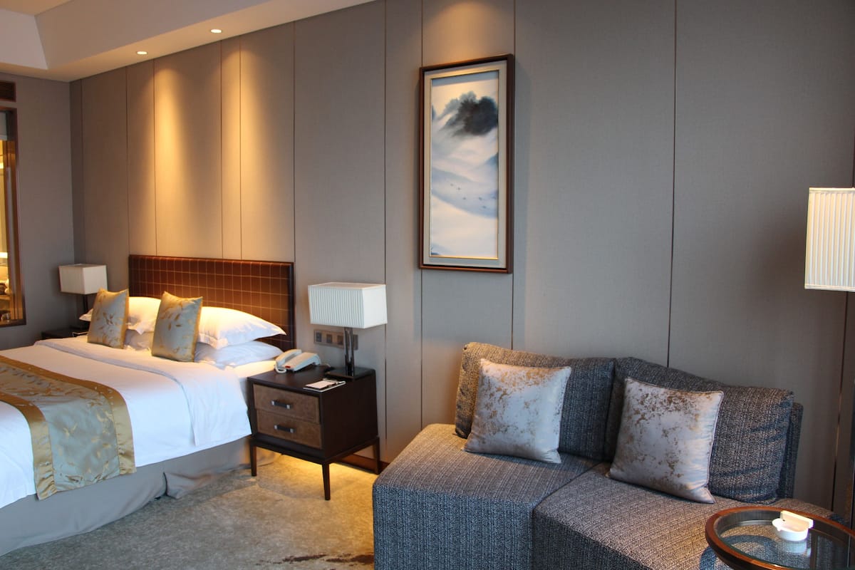 Una habitación de hotel con una cama, un sofá, una mesita de noche y una lámpara.