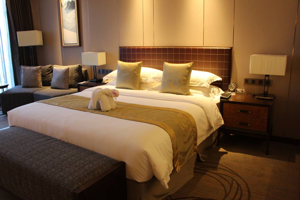 Habitación de hotel con una cama grande, un sofá pequeño, una mesita de noche con lámpara y otra mesita de noche también con lámpara.