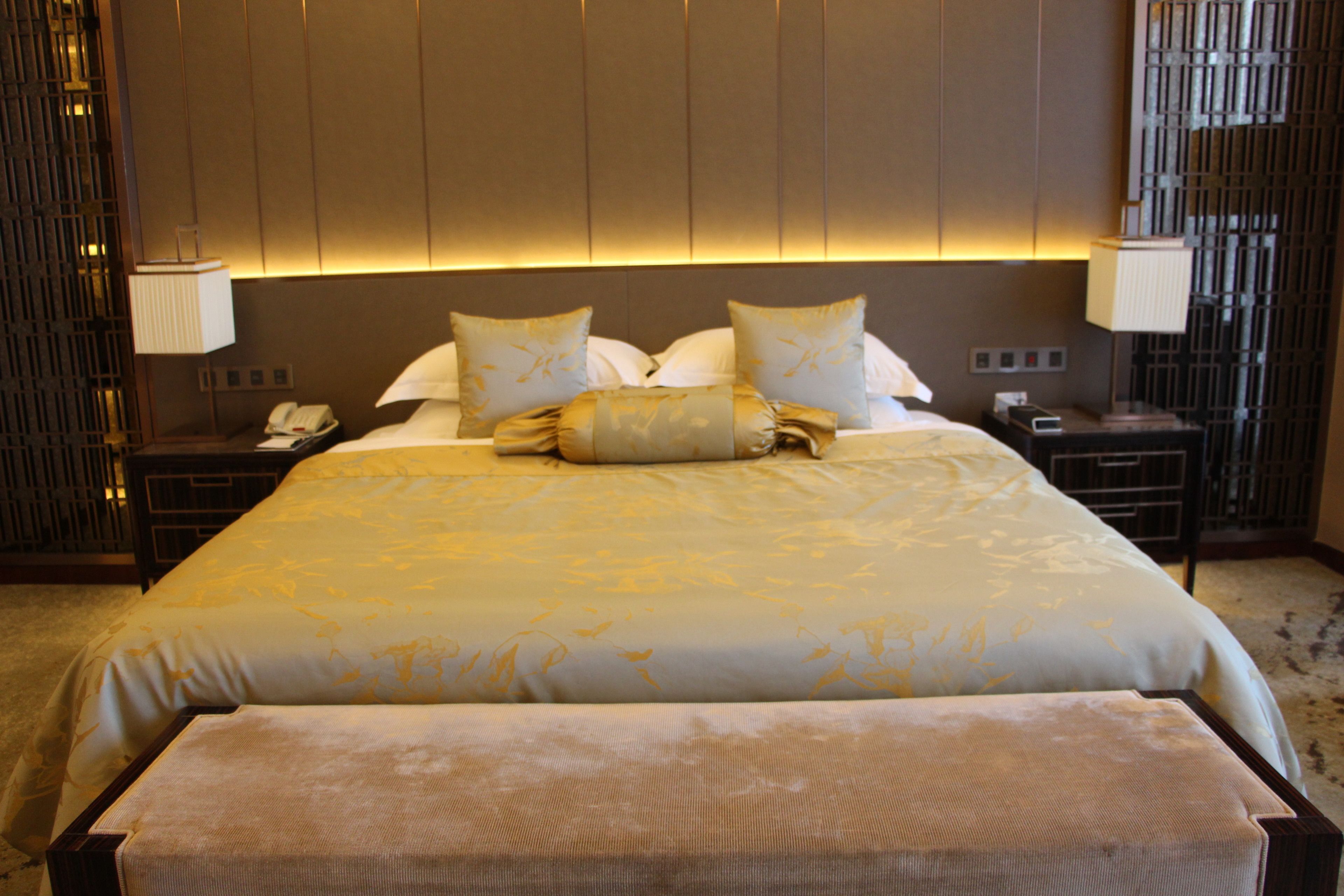 A hotel room with a large bed, two bedside tables, a nightstand, and a wall-mounted lamp.