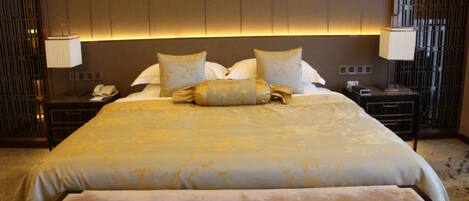 A hotel room with a large bed, two bedside tables, a nightstand, and a wall-mounted lamp.