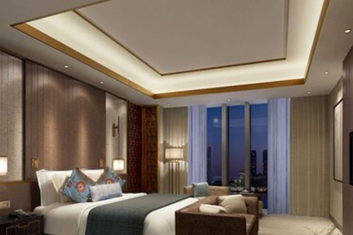Una habitación de hotel moderna con una cama grande, un sofá, una mesita de noche y vistas a la ciudad de noche.