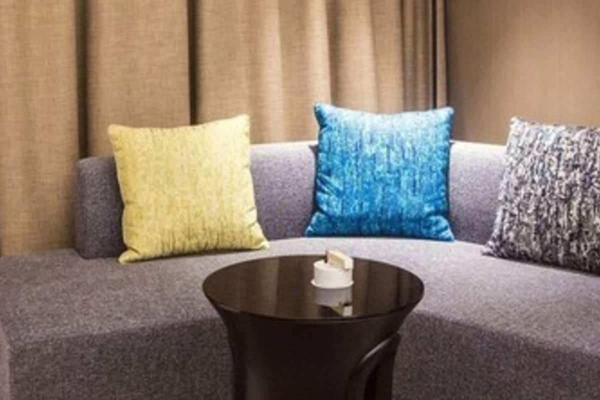 Una sala de estar moderna con un sofá gris, una mesa de centro negra y tres cojines decorativos en amarillo, azul y gris.