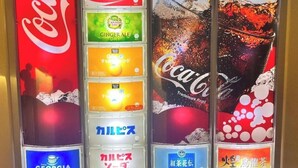 Ein Getränkeautomat mit verschiedenen Auswahlmöglichkeiten, darunter Coca-Cola, Ginger Ale und weitere Getränke.