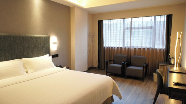 Una habitación de hotel con una cama grande, un escritorio con silla, una lámpara y una ventana con cortinas.
