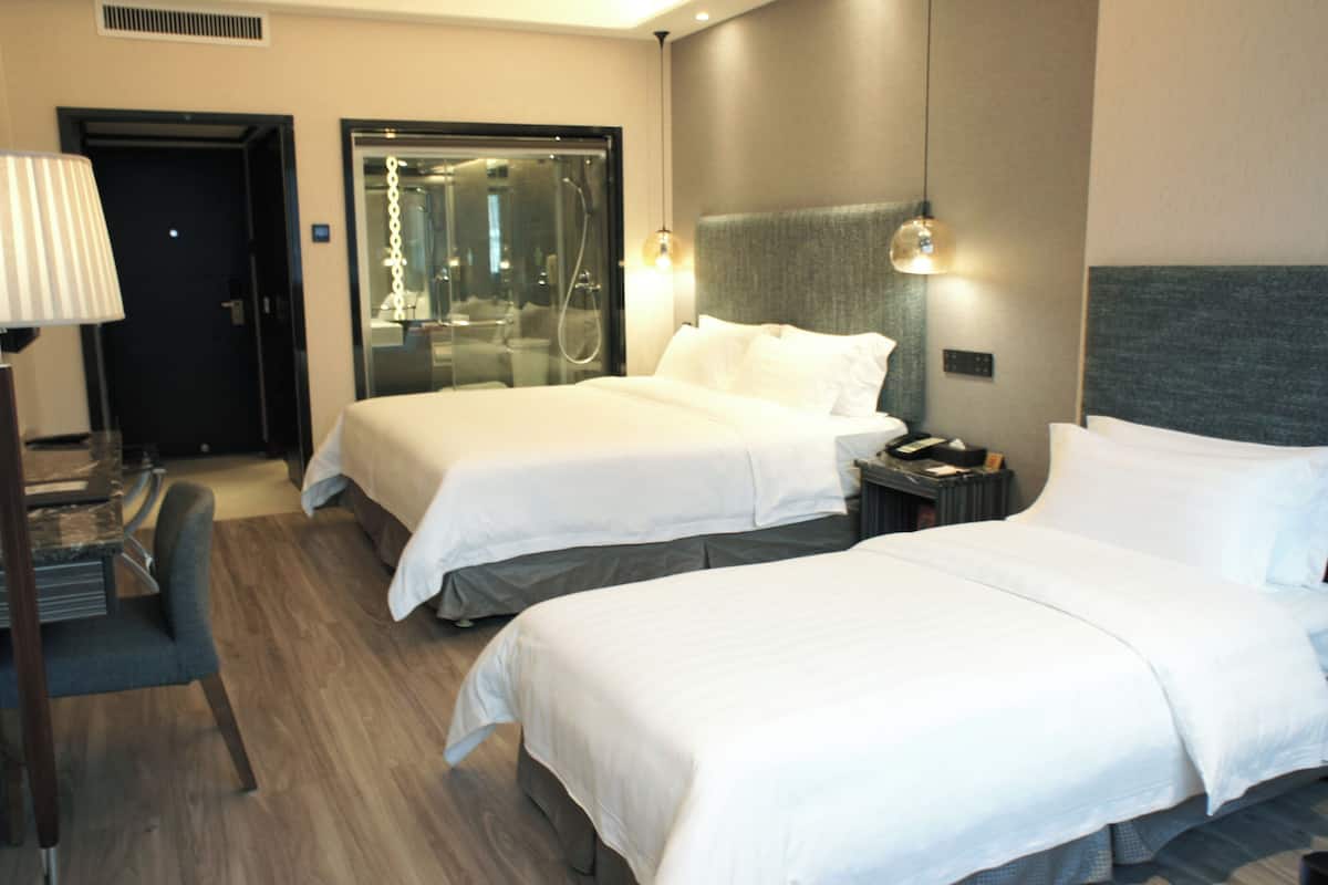 A hotel room with two beds, a desk, a lamp, and a mirror.