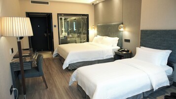 A hotel room with two beds, a desk, a lamp, and a mirror.
