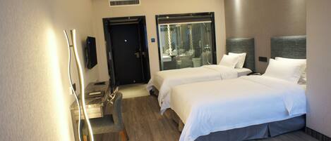A hotel room with two beds, a TV, a desk with a chair, and a shower area.