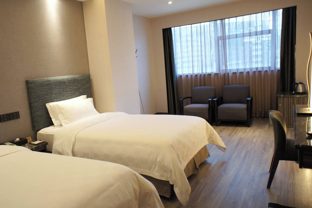 A hotel room with two beds, a desk, and a chair.