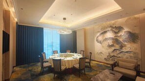 Comedor con mesa redonda dispuesta para seis personas, rodeada de sillas, una araña y un mural grande en la pared.